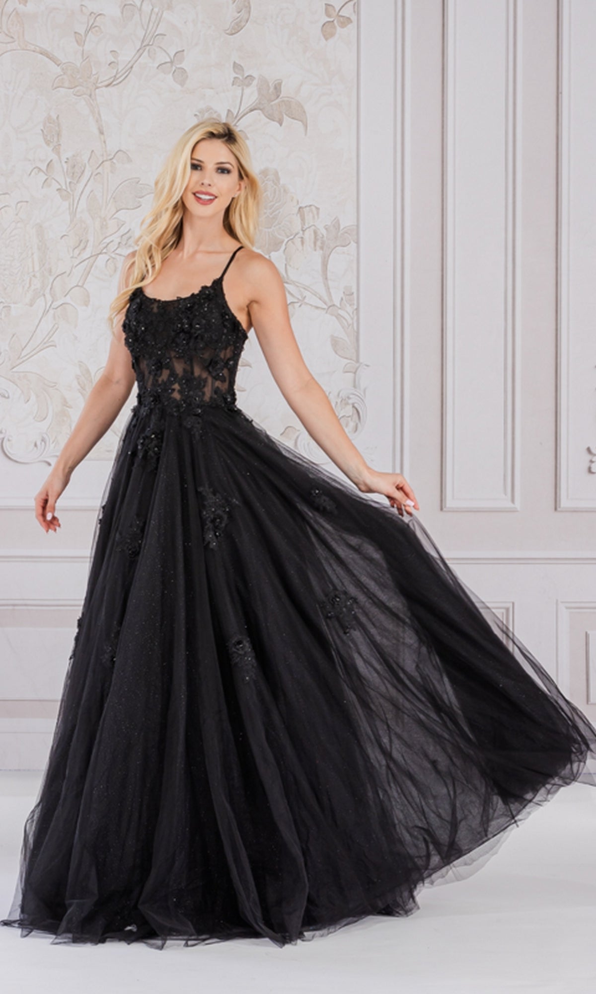 A woman wearing the Embroidered-Tulle Long A-Line Prom Ball Gown 7035, featuring a sheer bodice, stands in a white room with floral-patterned wallpaper.